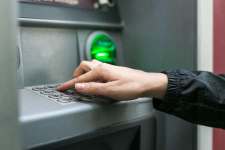 Closeup of female hands using smart phone while typing on ATM, bank machineの写真素材