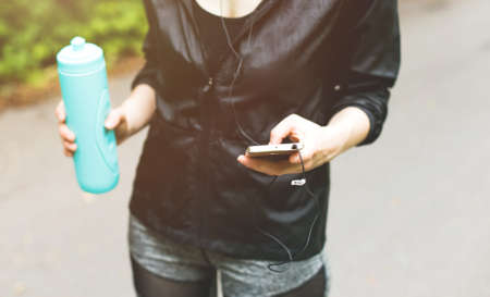 beautiful girl in sports uniform, doing exercises on the street, running around, drinking water and listens to music on the phone. Healthy way of life, an infused figure.の写真素材