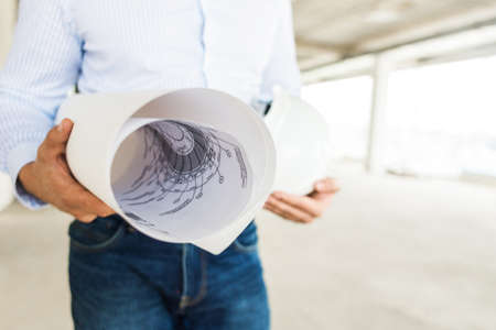 male engineer, architect in helmet at construction site holds drawing on paper in handsの写真素材