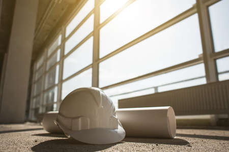white helmet, blueprints of a building on a construction site on a window backgroundの写真素材
