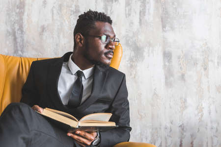 Attractive Afro American man in a business suit read a book in a stylish interior. businessman and company leaderの写真素材