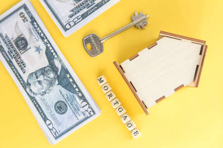 mortgage, loan and home purchase. Model of house, dollar bills, key on white and yellow isolated background. Free space for text, flatlayの写真素材