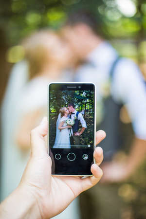 A photographer takes a picture on a mobile phone at a wedding. kiss bride and groomの写真素材