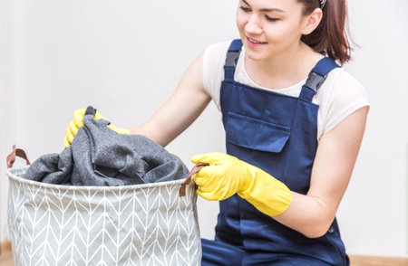 Cleaning service with equipment during work. women in uniform, overalls and rubber gloves woman puts dirty laundry in the basket, cleaning the apartment, washing machine. Isolated on white, free spaceの写真素材