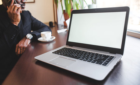 African American man sitting in a cafe, drinking coffee and working behind a laptop. Mock up screen.の写真素材