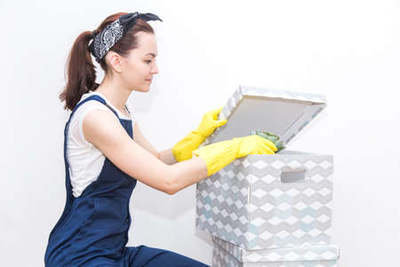 Cleaning service with equipment during work. woman in uniform, overalls and rubber gloves packs for moving to cardboard boxes. professional loader. transportation of fragile goods. free space for textの写真素材