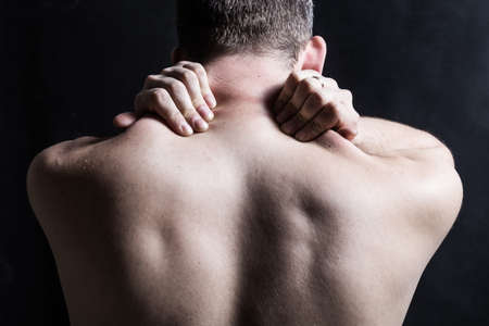 A man with pain in the back and neck. Close up of holding on the neck on a darkの写真素材