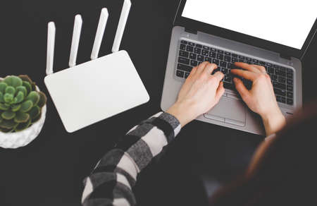 Girl using laptop with the phone in hand near white wi fi router in office.の写真素材