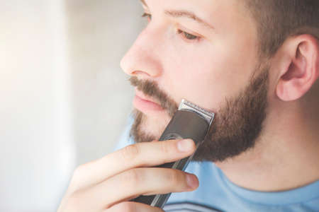 close up of a handsome young man shaves his beard with an electric razor. Skin irritationの写真素材