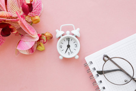 White table clock, alarm clock on a bright background, top view. Break at work in the office. Paper,...