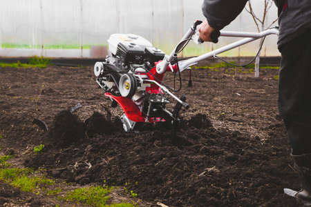 A man is a farmer plowing the land in the garden with a hand tractor cultivator.の写真素材