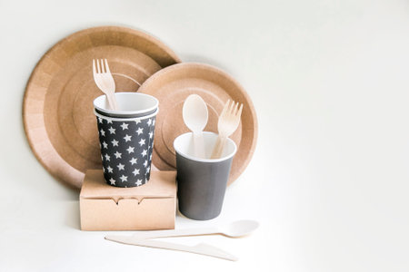 eco friendly disposable dishes made paper on white marble background. Draped spoons, fork, knives,...