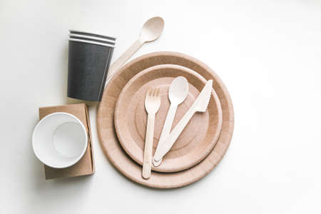 eco friendly disposable dishes made paper on white marble background. Draped spoons, fork, knives, plate with paper cups. recycling conceptの写真素材
