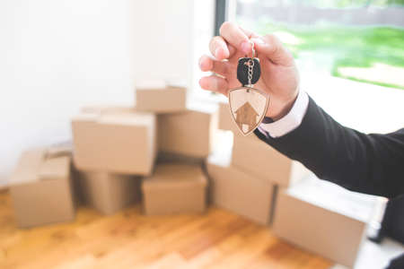 male realtor holds the keys to a new home. Moving day, cardboard boxes in new apartment.の写真素材