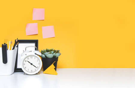 Office workplace, clock alarm, creative workspace on yellow wall. Mock up , free space for text on stickers and wallの写真素材