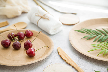 eco friendly disposable dishes made paper and bamboo on white marble background. Draped spoons,...