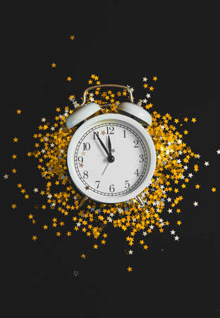 New Year Christmas Top view flat lay white alarm clock twelve covered golden stars confetti copy space black color paper background minimal style.の写真素材