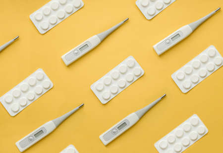 composition pattern from white pills and a thermometer top view on a yellow background.の写真素材
