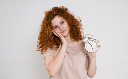 portrait of a beautiful woman with red curly hair holding an alarm clock. Sleep and wake up concept....