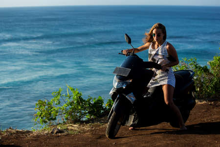 beautiful girl sitting on a motorcycle on a cliffの写真素材