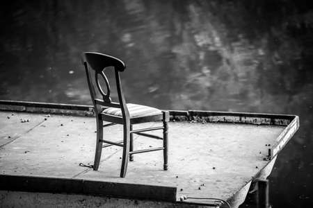 Black and white photography of lonely chair on a floating bridge at lake at evening. Lonely chair on pontoon near water.の写真素材