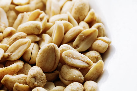 Fried salted nuts peanuts on a white background in a plate. Assorted snack pile of nuts. Abstract...