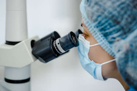Researcher gaze into the eyepieces of a large laboratory microscope against a blurred background of a scientific laboratoryの写真素材