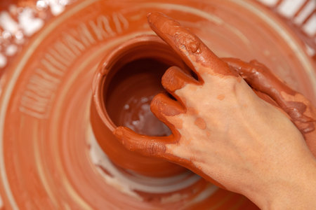 The process of making pottery on a pottery wheel in a workshop. Potter's hands close up (Top view)