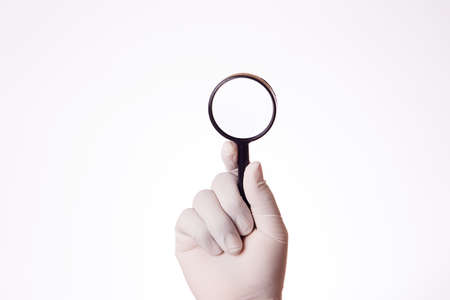 A man's hand with a latex glove uses a magnifying glassの写真素材