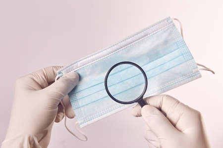 A man's hand with a latex glove uses a magnifying glass with a surgical maskの写真素材