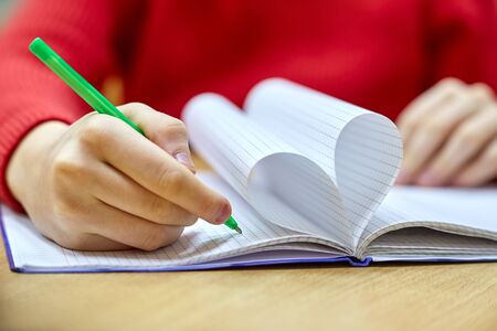 female hand writing on a blank piece heart-shaped Notepad with penの写真素材
