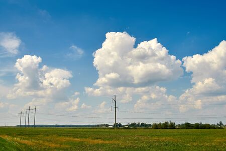 Huge white clouds in the sky over green fields, trees, forests. Electric polesの写真素材