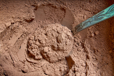 Cocoa powder in a spoon on cocoa powder background. Close-up.