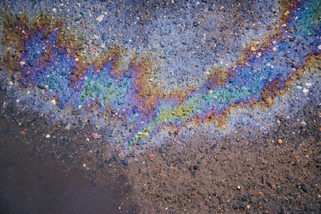 Oil stain on wet asphalt caused by a leak under a car or truck.Environmental petrol oil pollution.