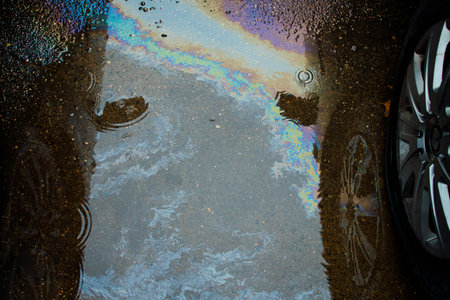 Colorful gas stain on wet asphalt. Oil stain caused by a leak under a car or truck.