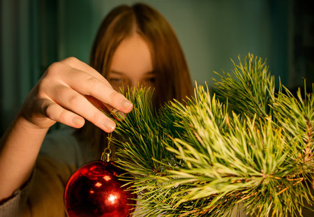 A female hand hangs a red Christmas tree toy on a Christmas tree branch. Preparing for the New Year concept. Soft selective focusの写真素材