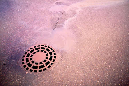 Oil slick on the asphalt road background drains into the storm drain.Water pollution environmental problemsの写真素材