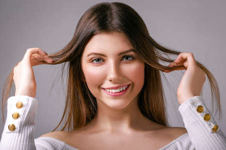 Delighted young girl with loose hair stands on a gray background looking happily at the cameraの写真素材