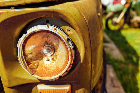 Part of the front of an old rusty green car with a broken headlight
