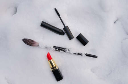Makeup accessories, cosmetic products on snow background. Stylish christmas lipstick and mascara with face brush with space for text.の写真素材