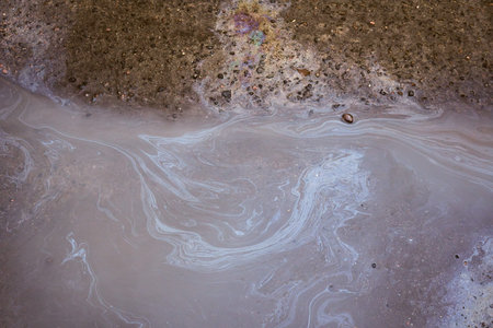 Gas stain on wet asphalt caused by a leak under a car or truck, abstract background