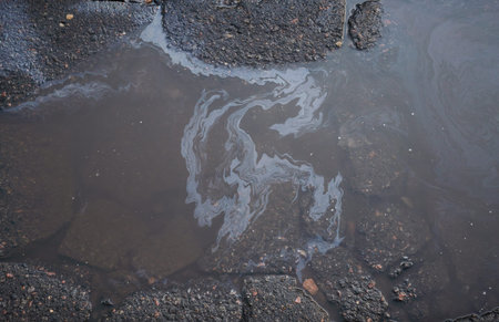 An oil stain in a puddle against the background of cracked asphalt and sky reflections, iridescent...