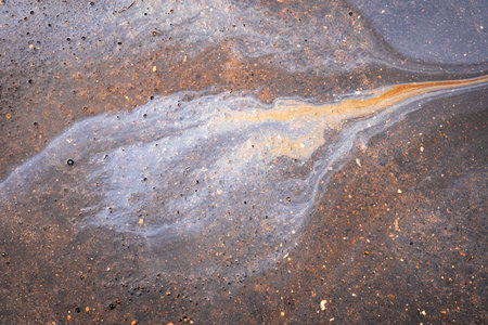Water with patches of gasoline and oil. Spilled oil on the asphalt road background.