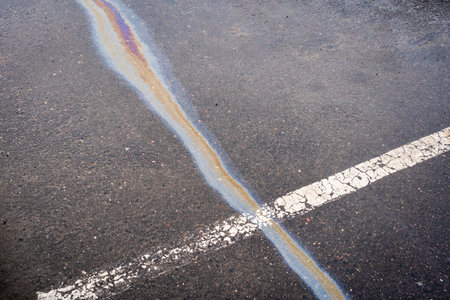 After rain on wet pavement, an iridescent spill of oil or gasoline crosses the dividing line.の写真素材