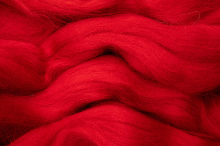 Red merino wool for felting as background. The stripes of red yarn folded in abstract order.