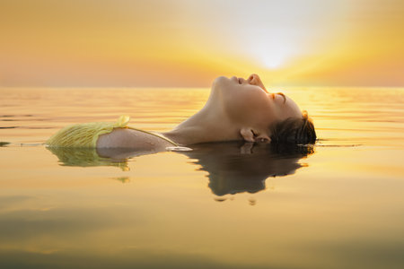 Girl lies on the water in the rays of the rising sun. Beautiful girl is relaxing in the, swim and relax.の写真素材