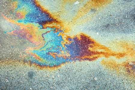 A puddle of spilled gasoline or oil product on the road. Environmental pollution concept. Gasoline...