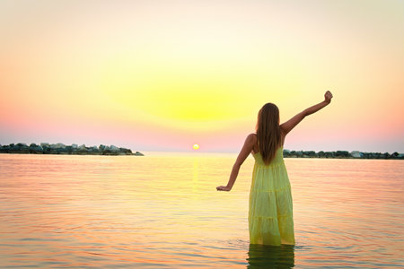 A young woman meets the sunrise by going into the sea.の写真素材