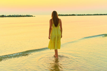 A young woman walks along the beach at dawn.の写真素材