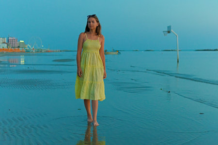 A young woman in a yellow dress, watching the sunrise, walks along the beach.の写真素材